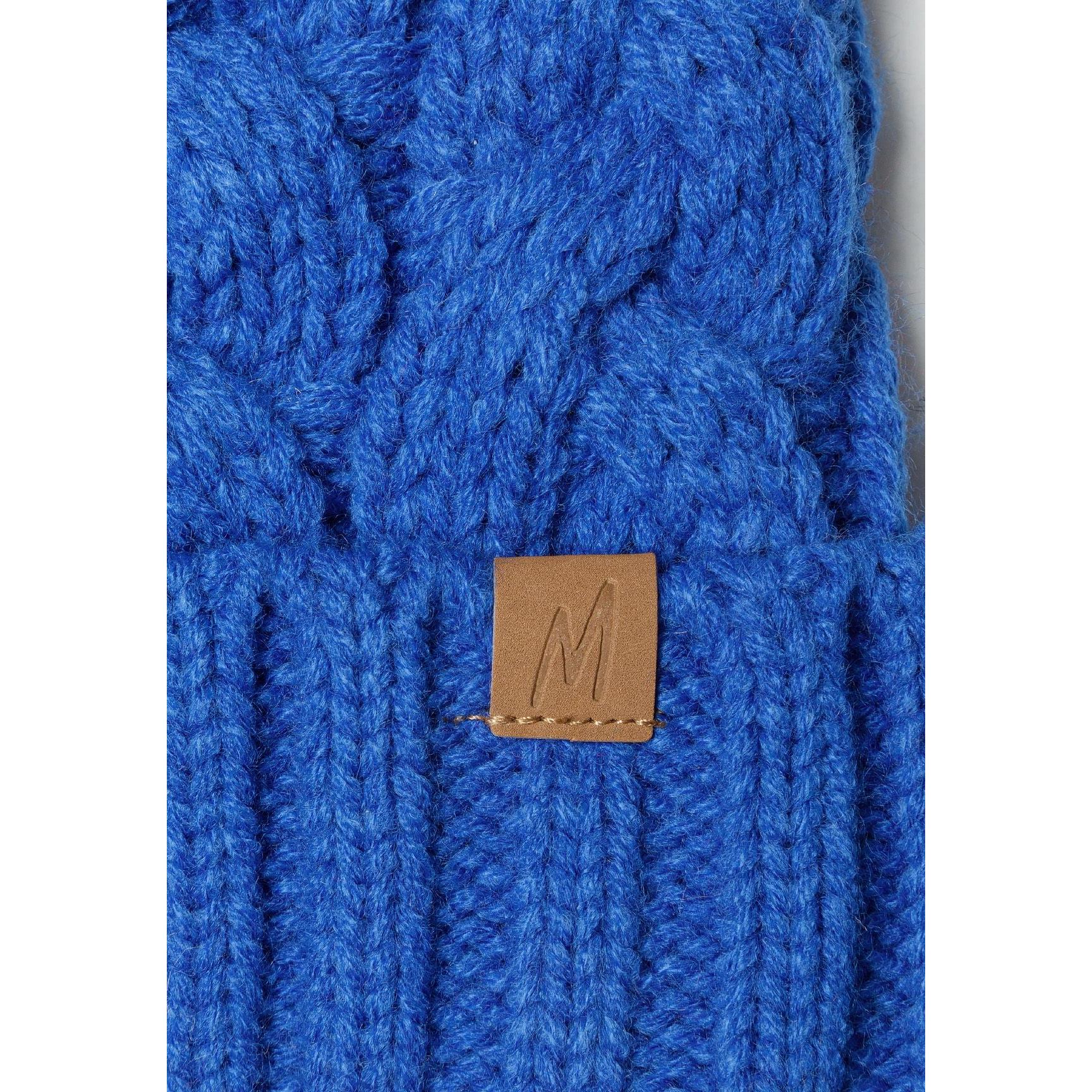 Close-up detail of cable knit texture and brown leather Minoti label with embossed M letter on cobalt blue beanie