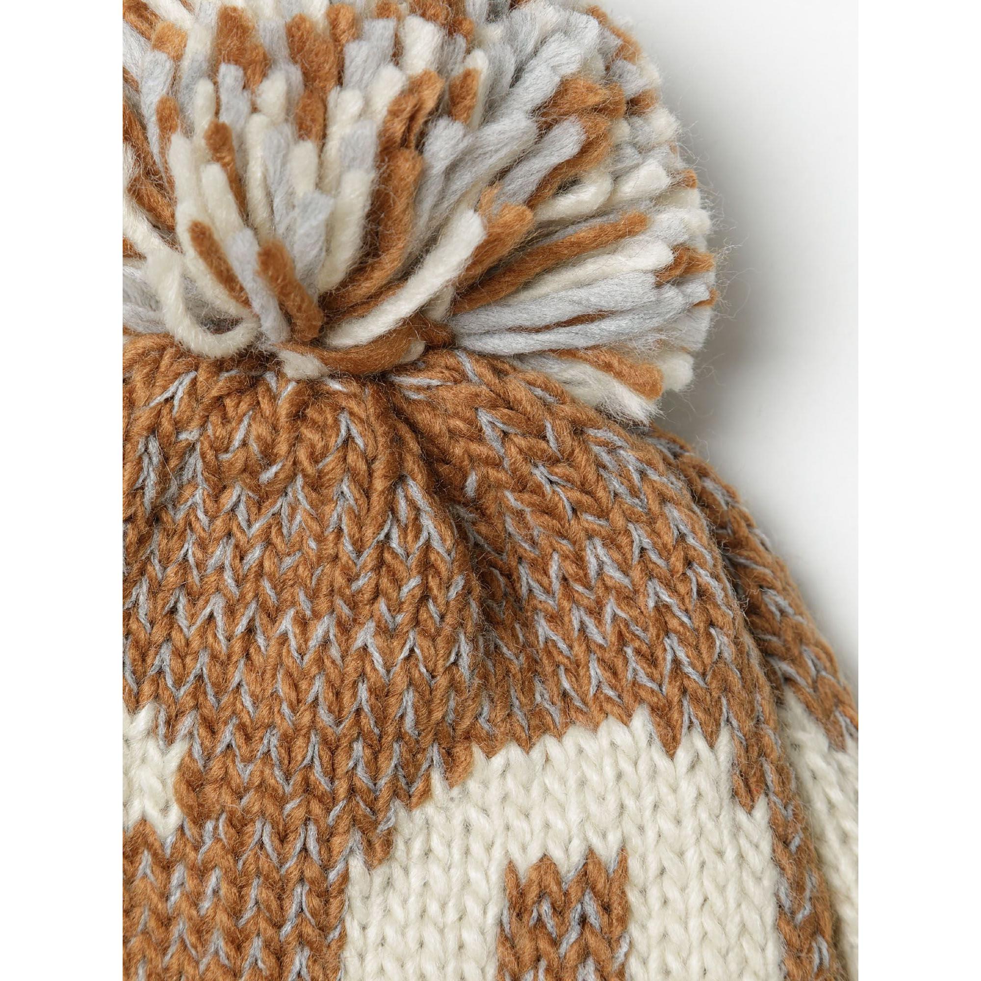 Close-up detail of beige jacquard beanie showing knit texture and multicoloured pom pom with brown, cream and grey yarn strands