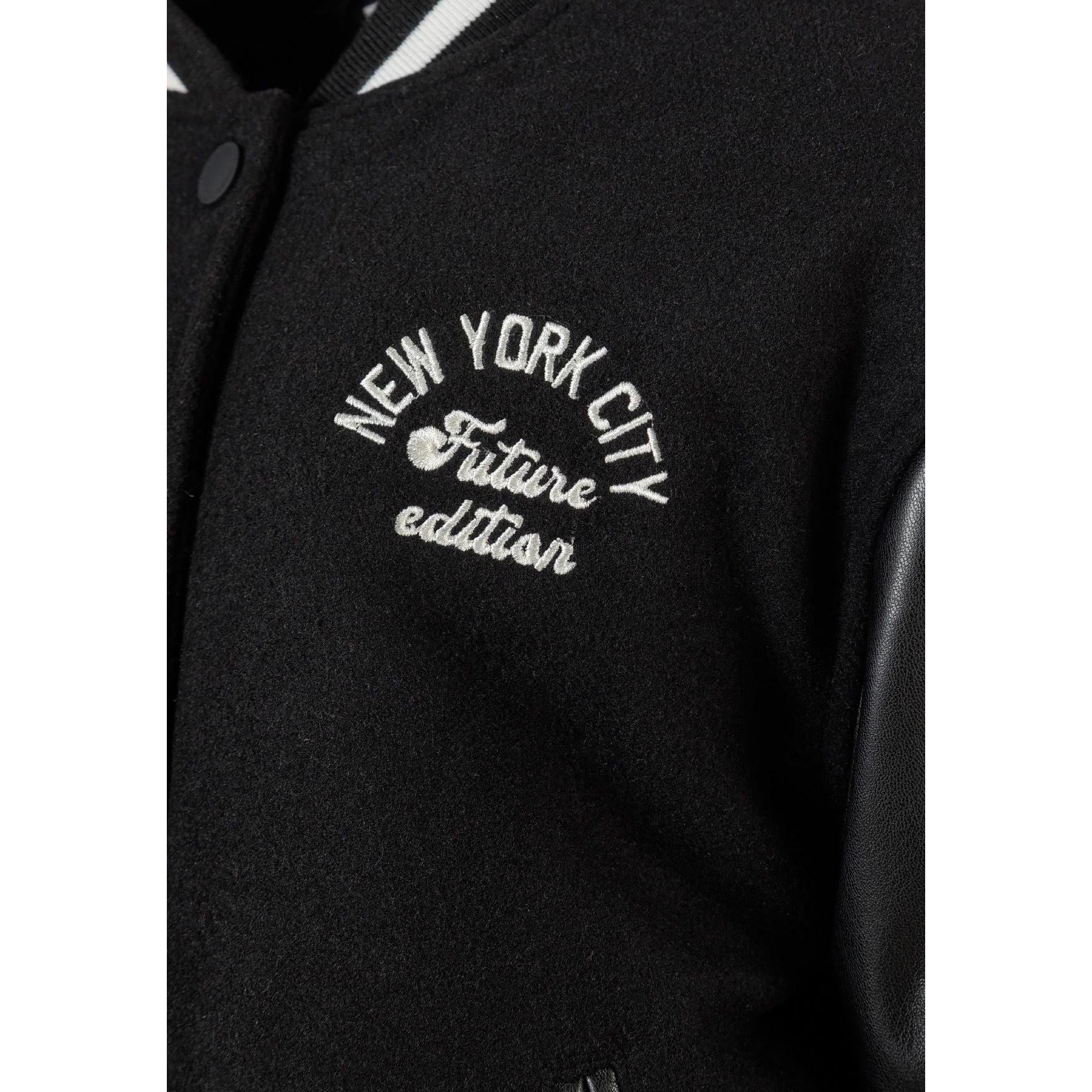 Close-up detail of black jacket showing side pocket with faux leather trim and felt body texture