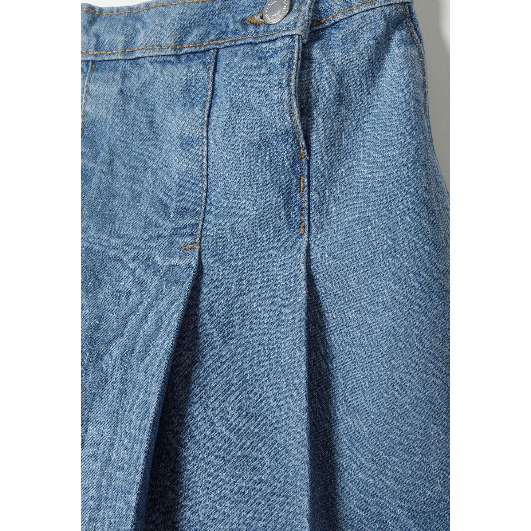 Close-up detail of navy denim skirt showing pleated construction and button fastening at waist