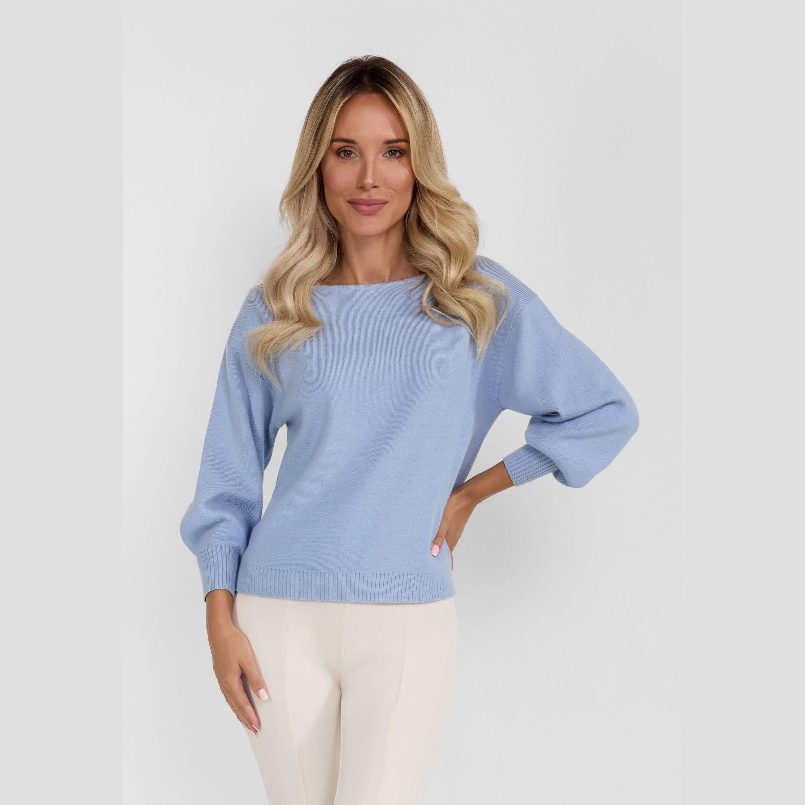 Woman wearing light blue boat neck jumper with long sleeves and relaxed fit, paired with cream trousers against white studio background