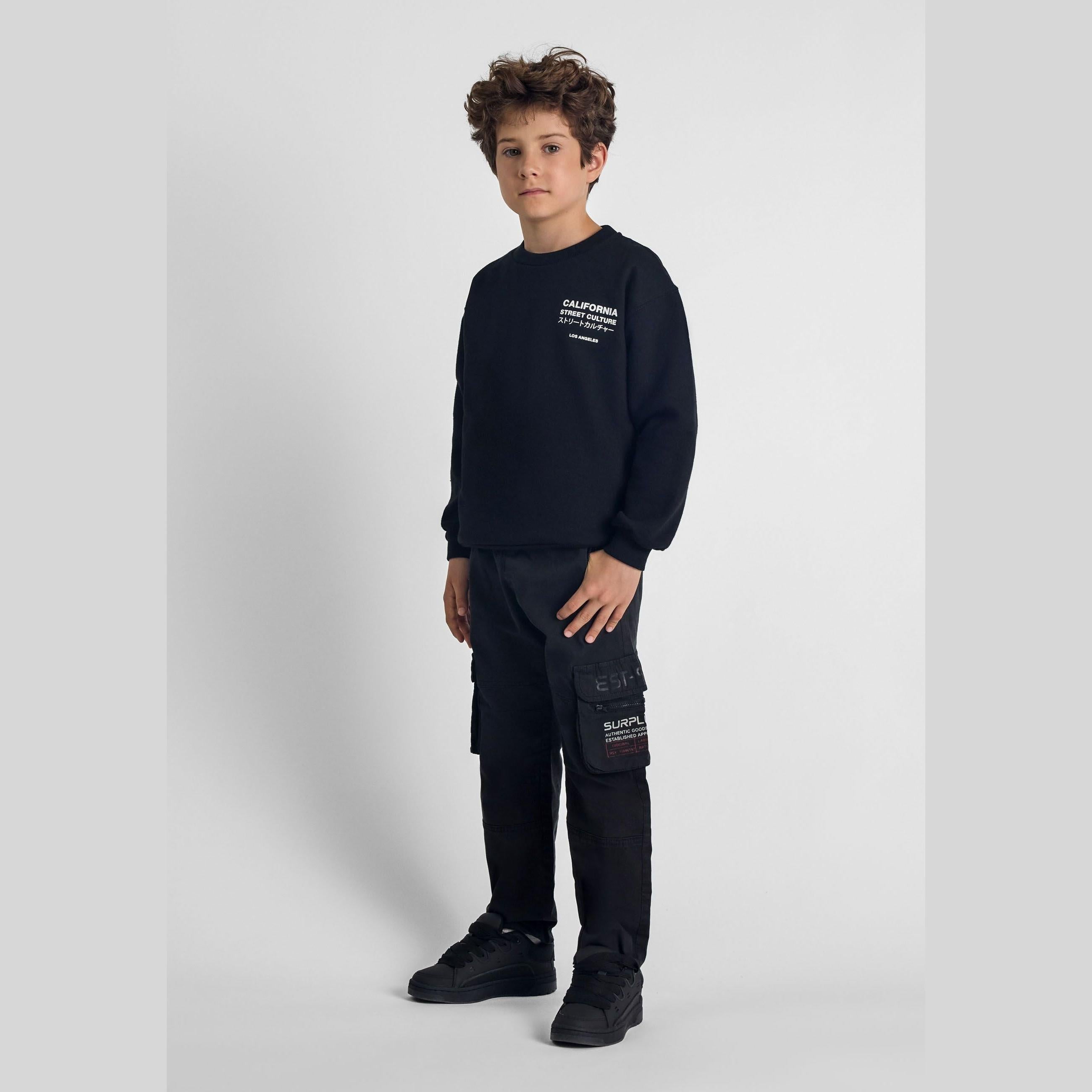 Boy wearing black cargo trousers and matching sweatshirt against white background, showing full outfit styling