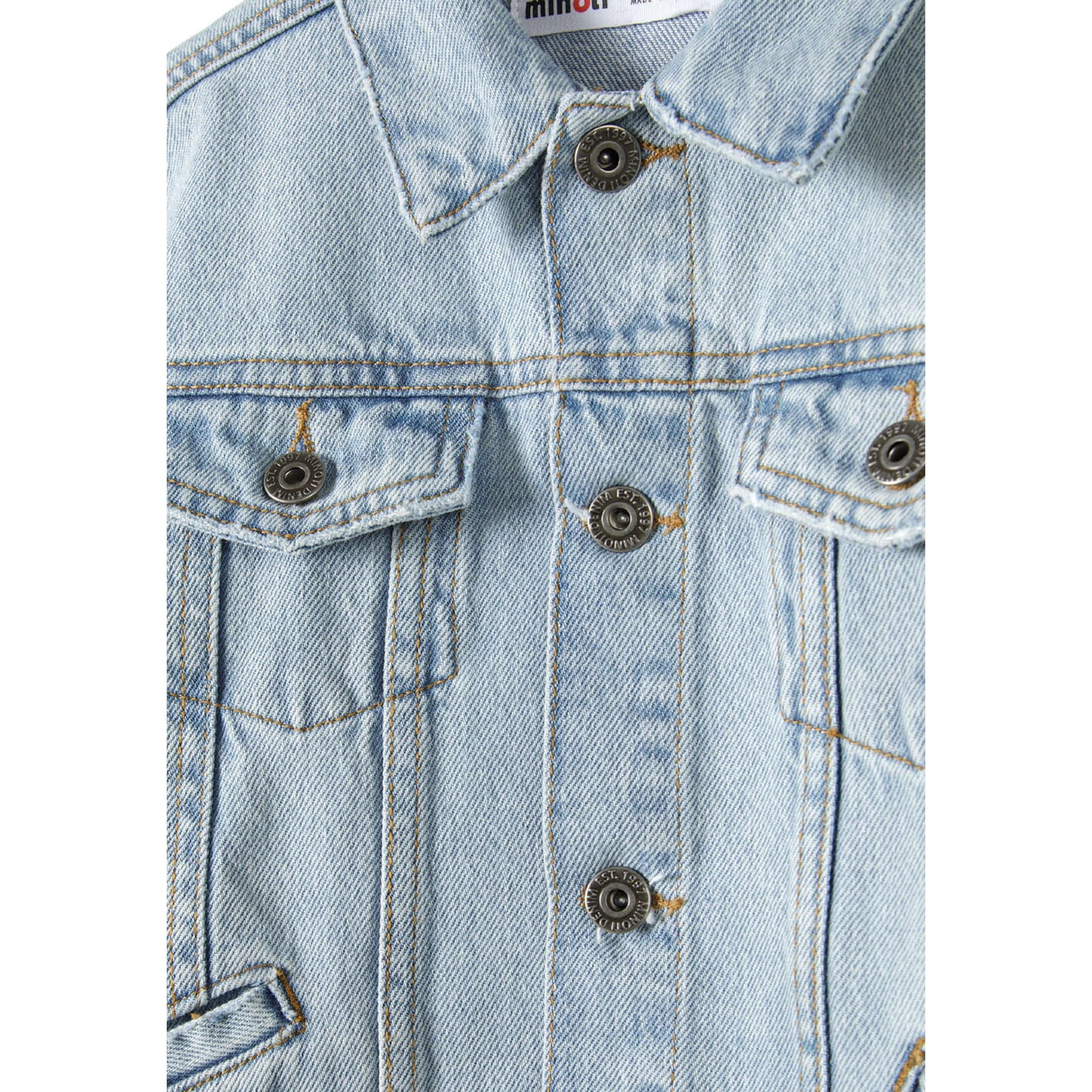 Close-up detail of light blue denim jacket showing collar, chest pockets, metal buttons and Minoti brand label