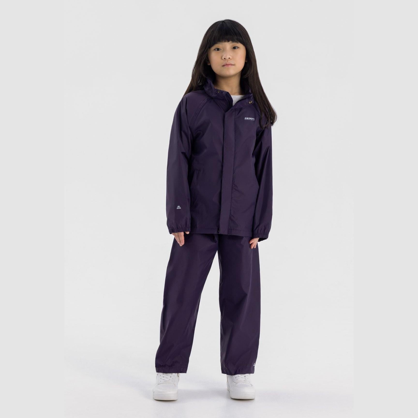 Young girl wearing purple waterproof overpants set with matching jacket, standing against white background, full body view showing complete rain protection outfit