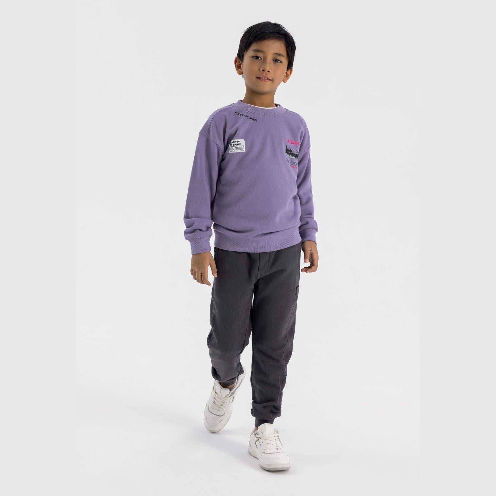 Boy wearing oversized lilac crew neck sweatshirt with skate graphics and dark joggers against white background