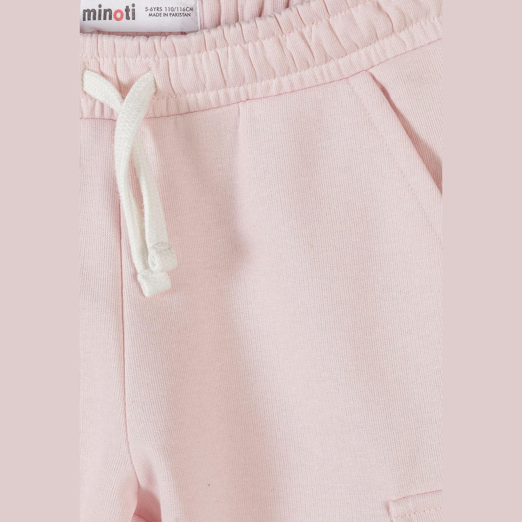 Close-up detail of light pink joggers waistband showing Minoti size label, elasticated waist with white drawstring ties, and fabric texture on pink background