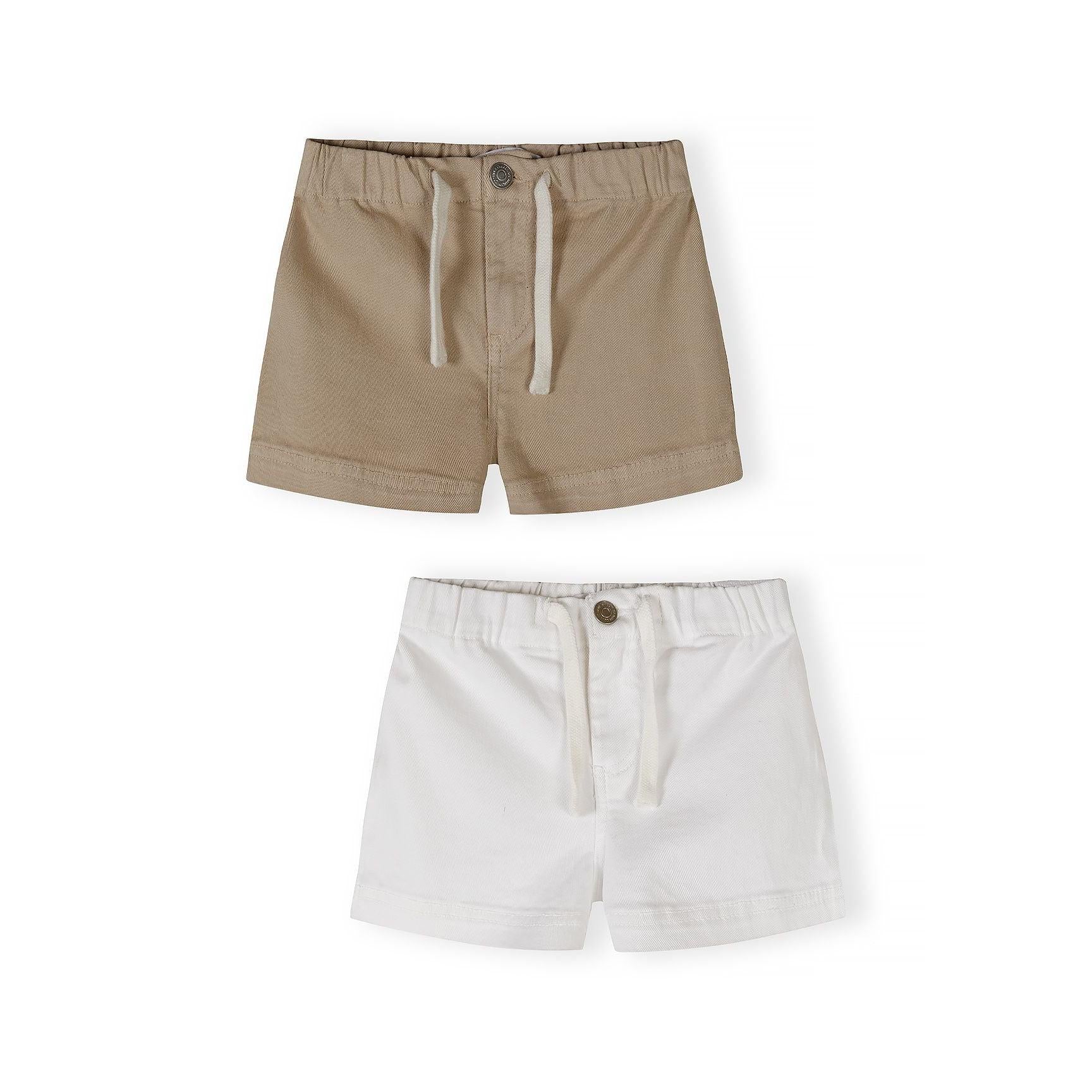 Two pairs of twill shorts on white background - beige shorts with white drawstring ties at top, white shorts with button fastening below