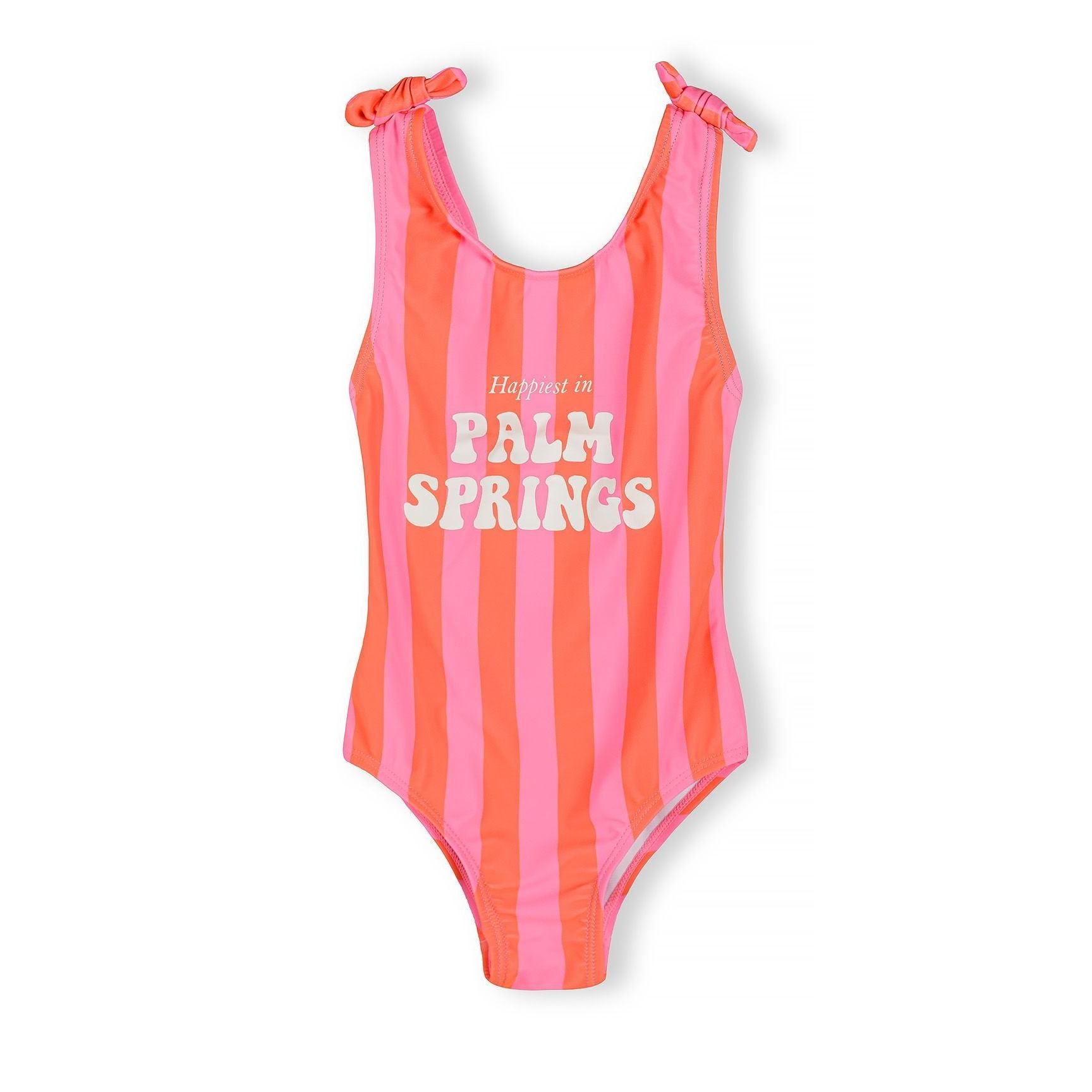 Pink and coral striped one-piece swimsuit with white 'Happiest in Palm Springs' text, featuring bow-tie shoulder straps, displayed flat against white background