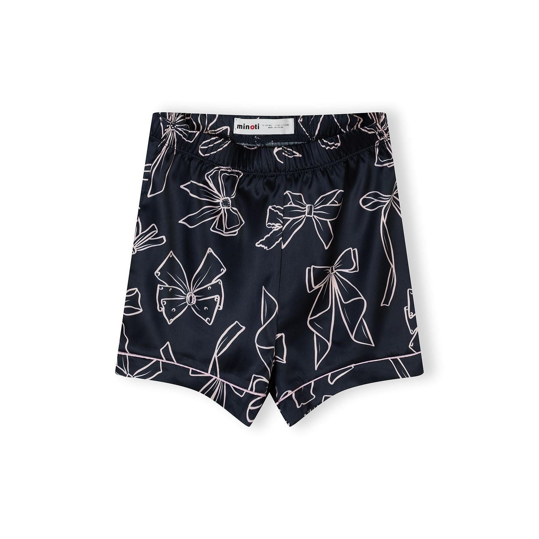 Close-up of navy satin pyjama shorts with white bow print pattern and elasticated waistband, showing Minoti label
