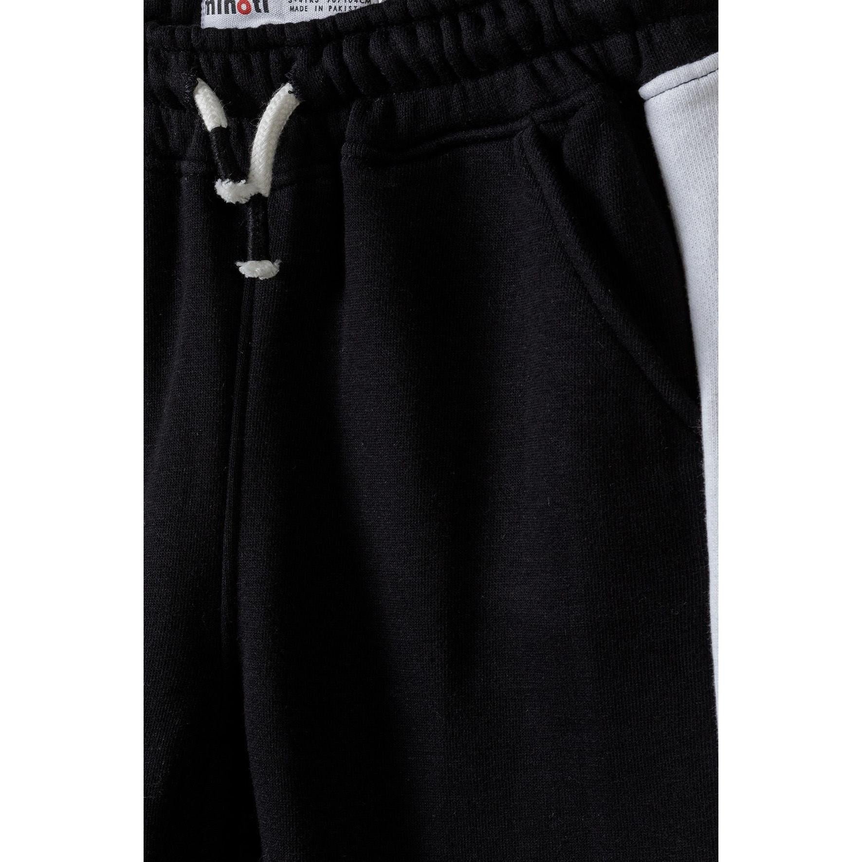 Close-up detail of black joggers waistband showing white drawstring with tipped ends and Minoti label