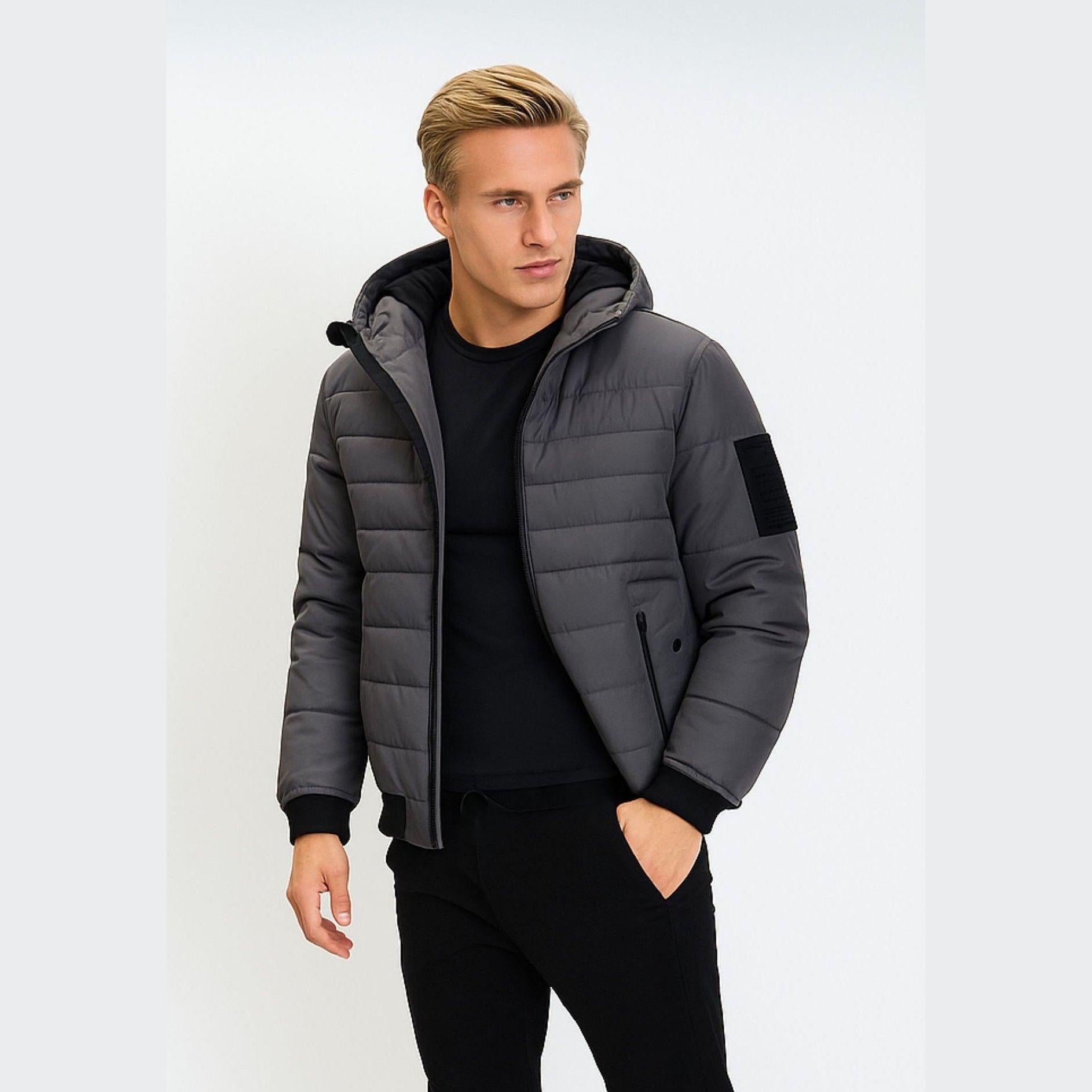 Model wearing grey hooded padded jacket with black ribbed trim, standing against white background