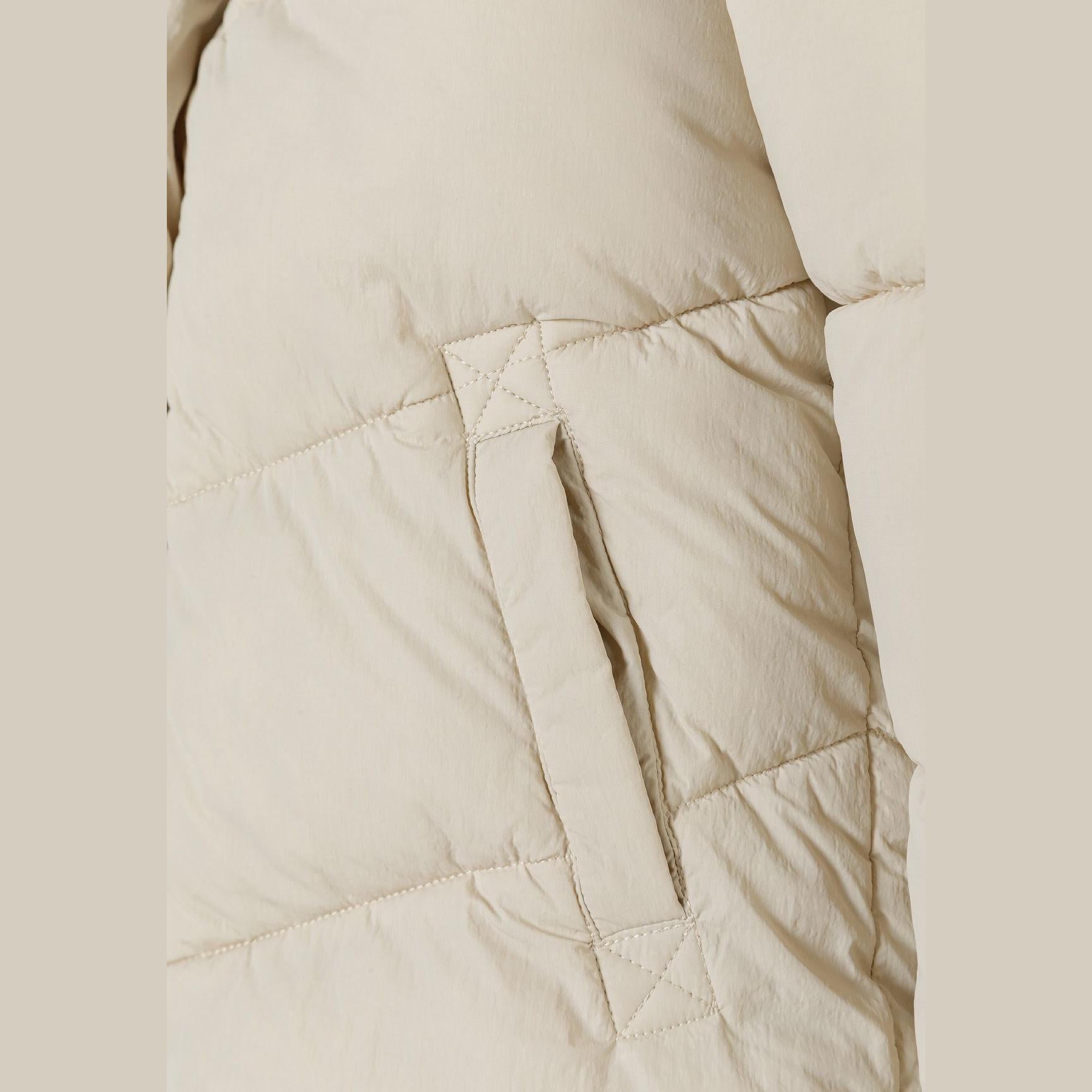 Close-up detail of circular embroidered patch with heart design and text on beige quilted puffer jacket fabric