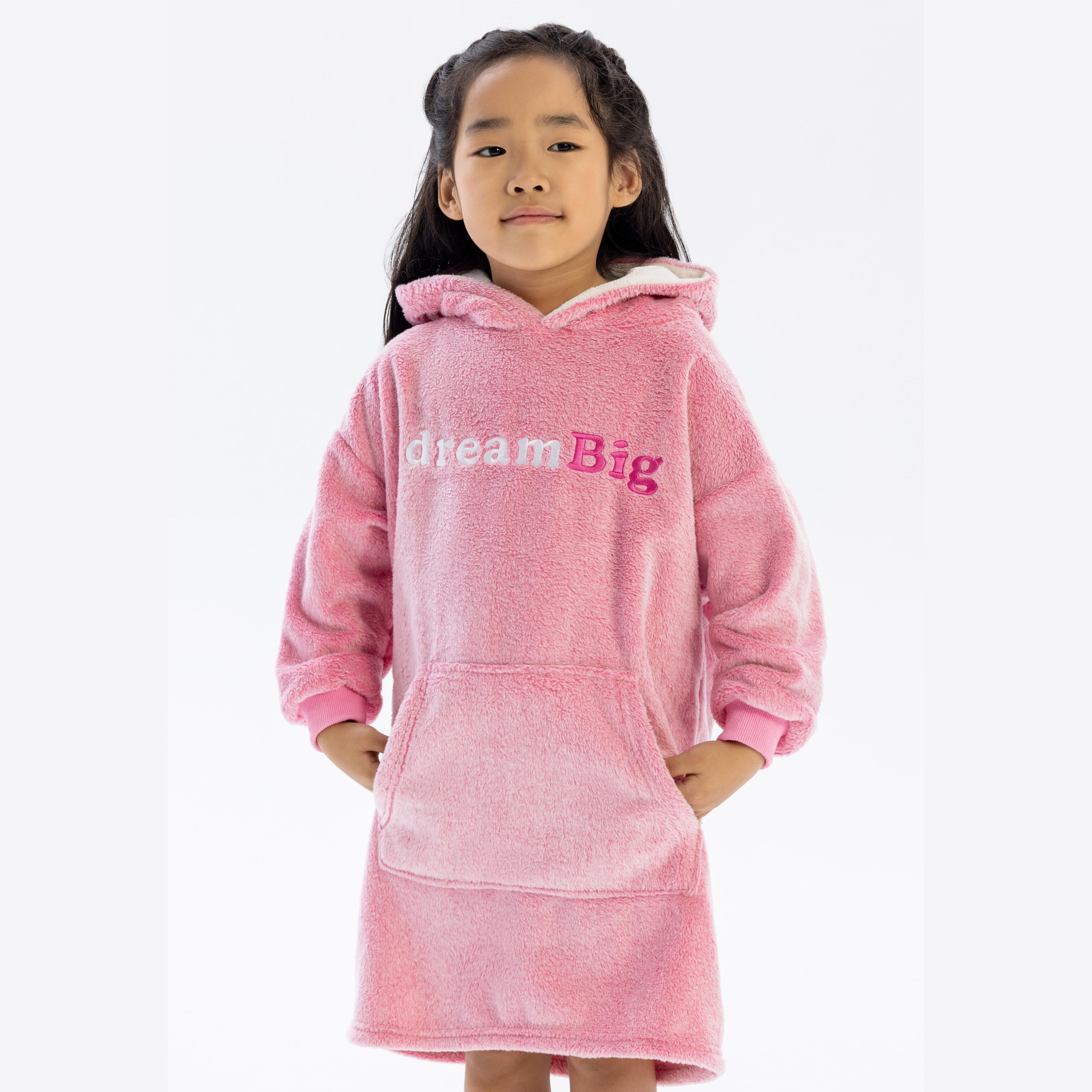 Young girl wearing oversized pink teddy fleece hoodie with 'dream Big' text, standing against white background with hands in front pocket