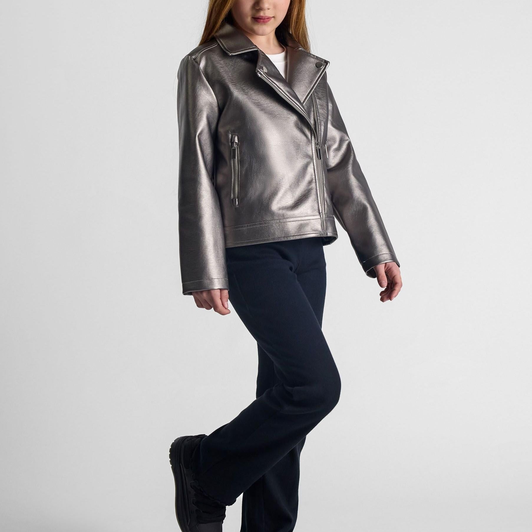 Girl wearing silver metallic biker jacket with dark jeans, showing diagonal zip closure and structured lapel collar against light background