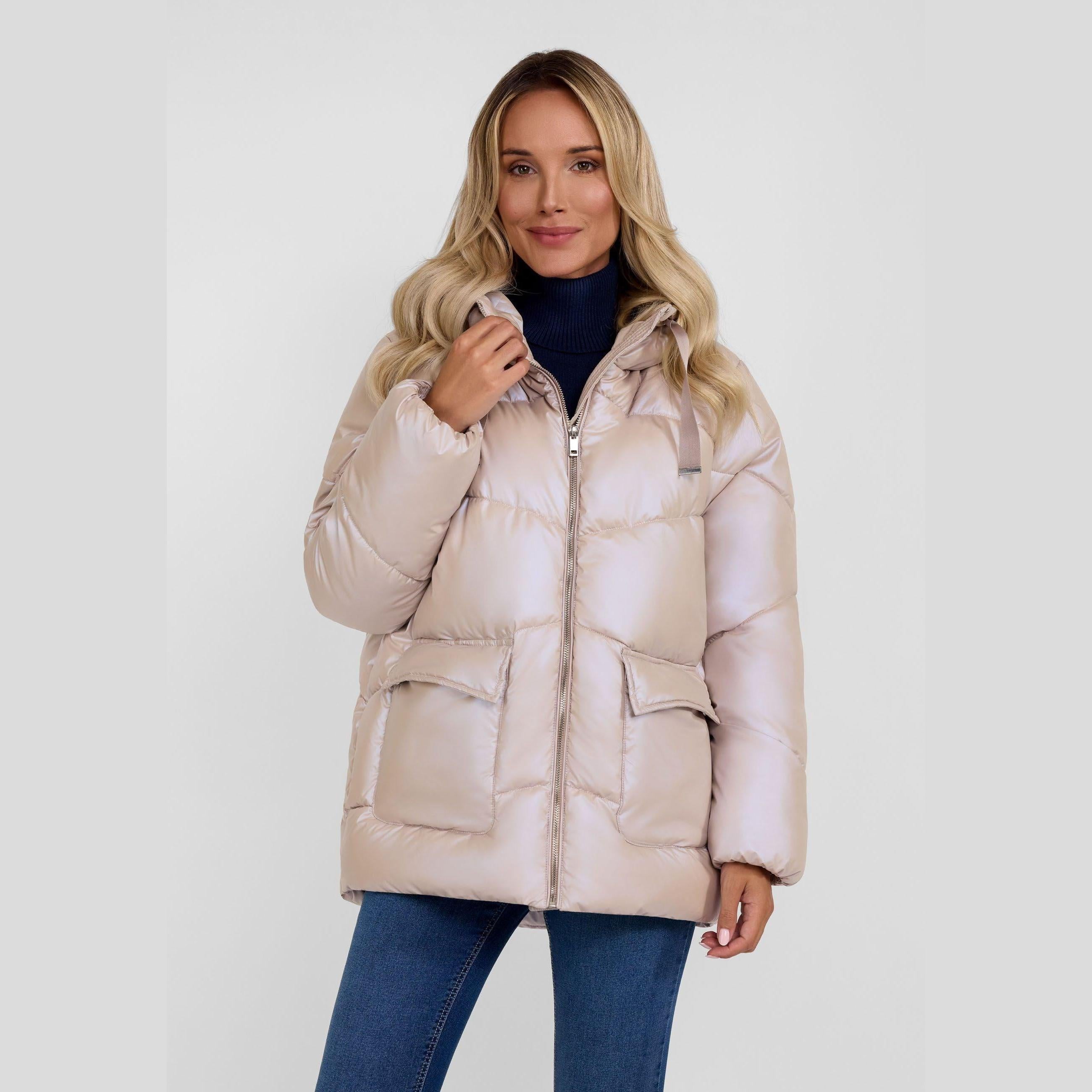 Woman wearing beige quilted puffer jacket with hood, paired with dark jeans against white background
