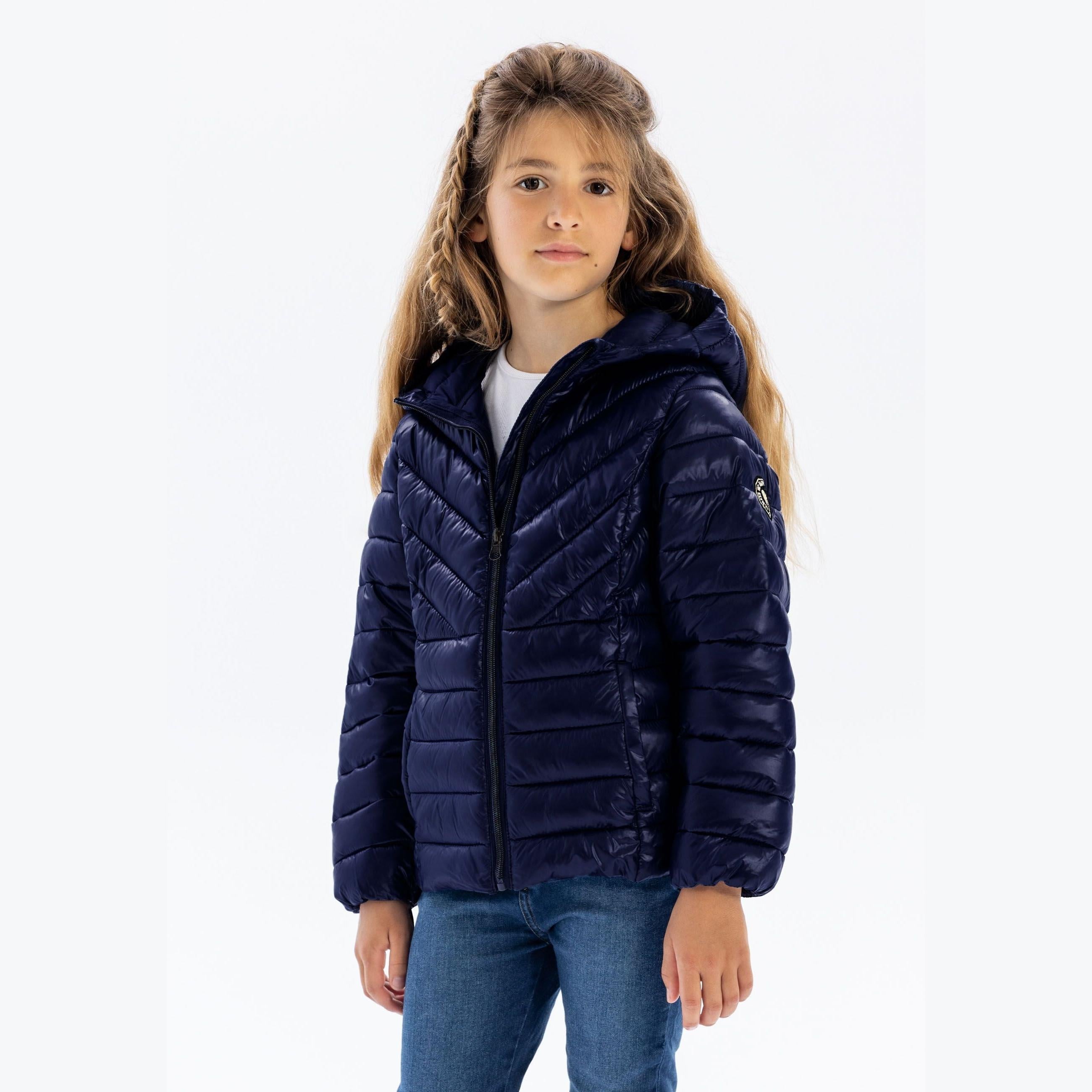 Young girl wearing navy quilted hooded jacket with jeans against white background, front view showing full zip closure and relaxed fit