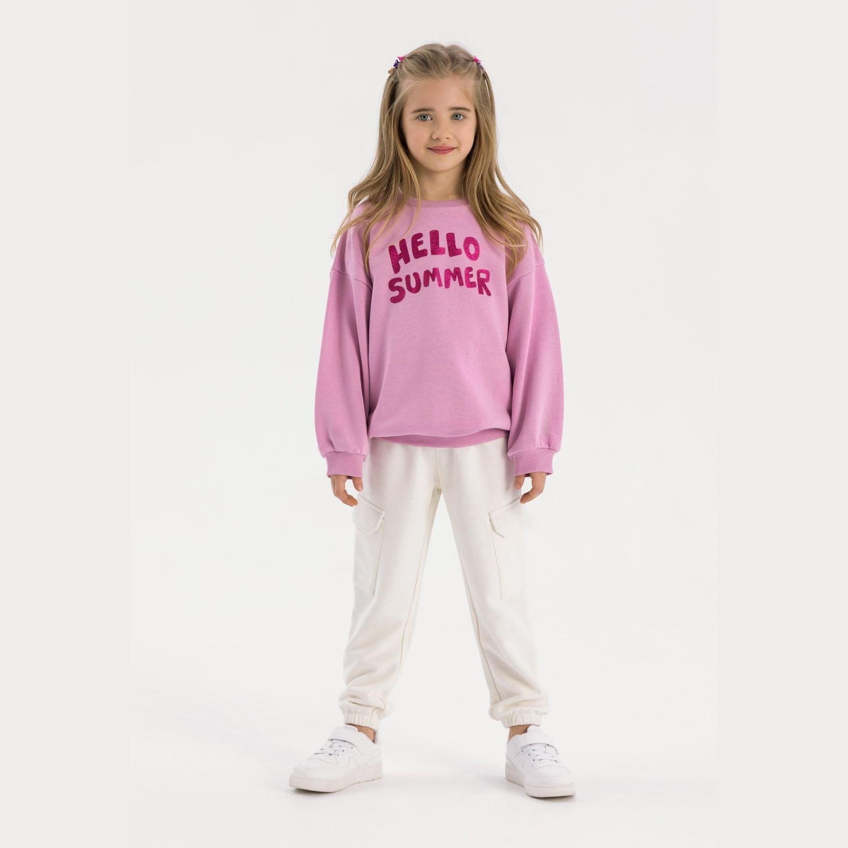 Young girl wearing white fleece cargo joggers with pink sweatshirt standing against white background
