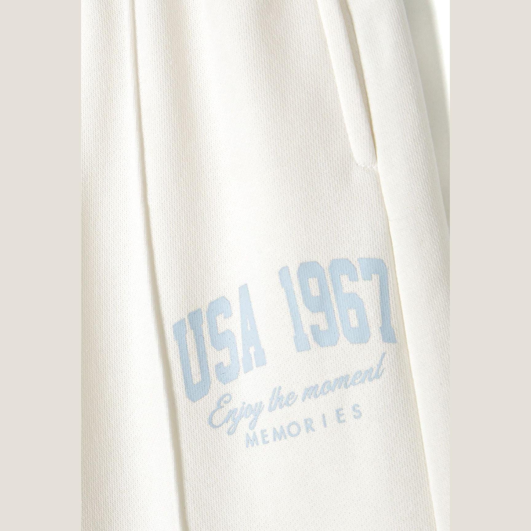 Close-up detail of cream joggers showing blue vintage-style text print reading 'USA 1967' with memories script text
