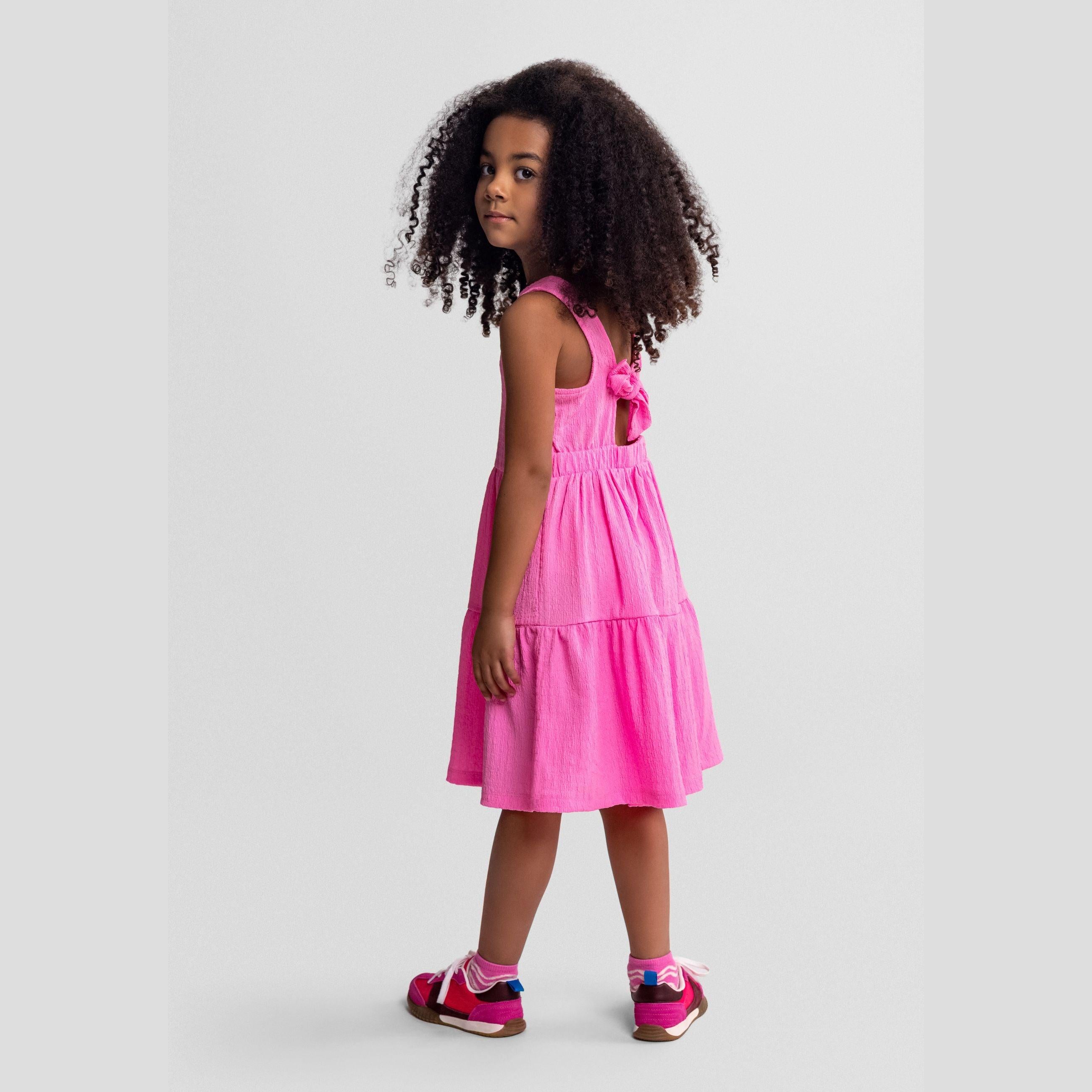 Bright pink tiered dress laid flat on white background showing sleeveless design and three-tier ruffle construction