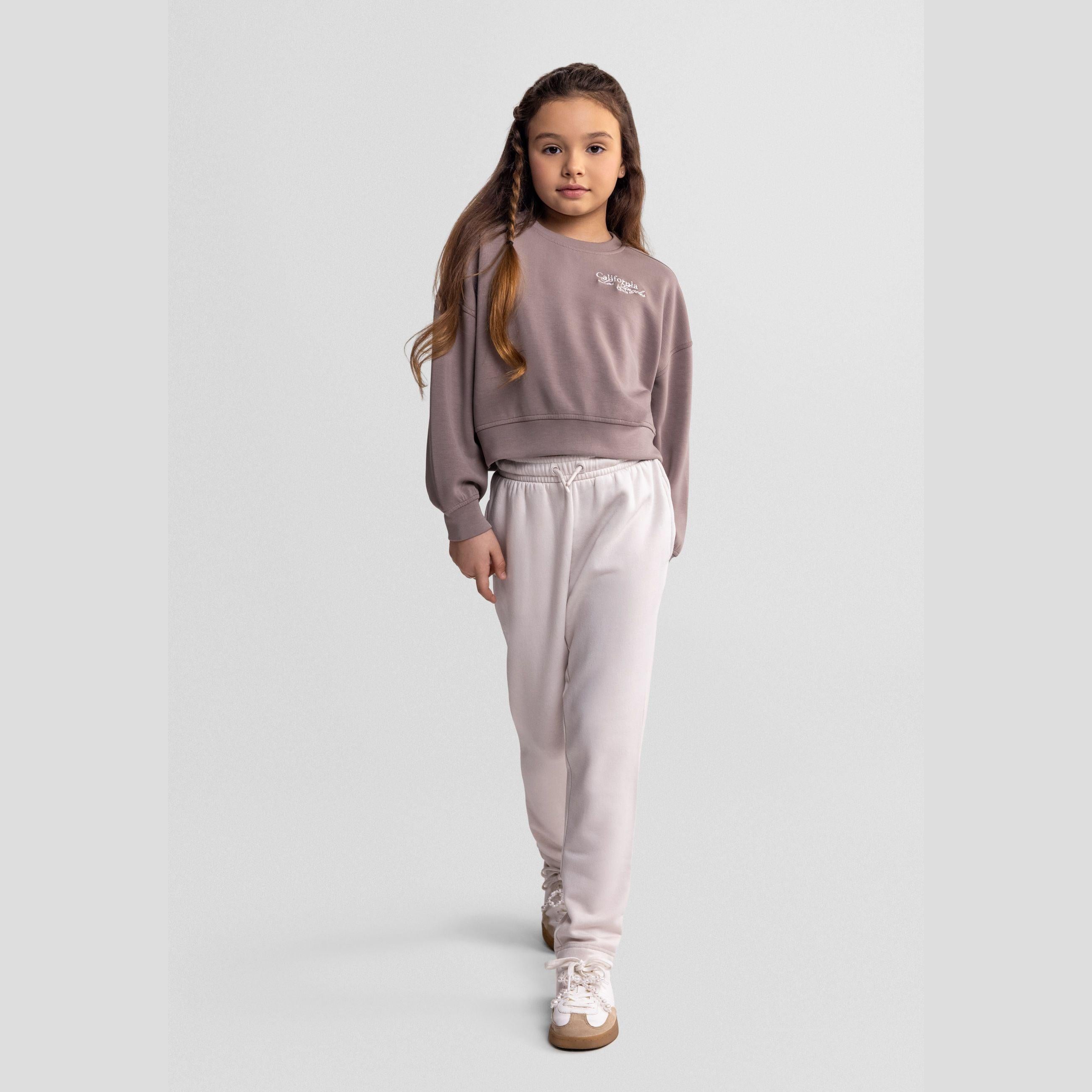 Girl wearing wide leg joggers in off-white with matching sweatshirt, full body pose against neutral background