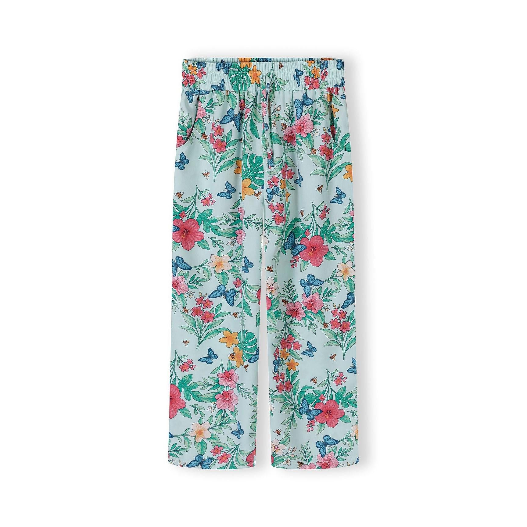 Close-up detail of mint tropical print pattern on wide-leg trousers showing colorful hibiscus flowers, butterflies and tropical leaves