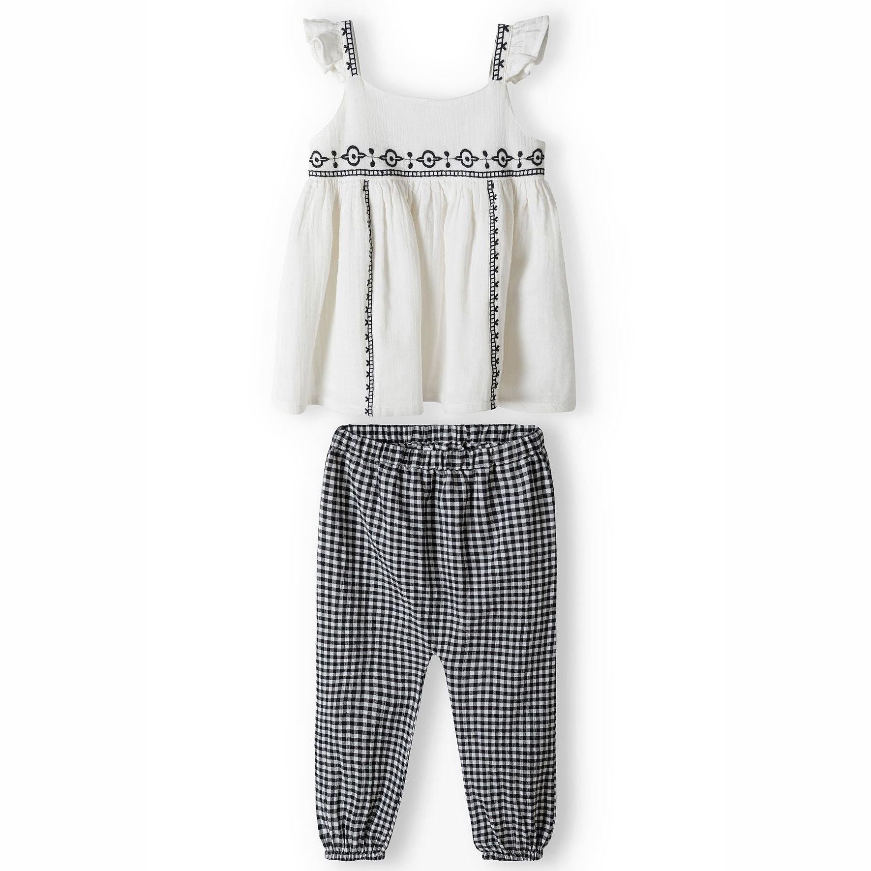 Flat lay of cream sleeveless top with decorative black embroidered trim and button front closure on white background