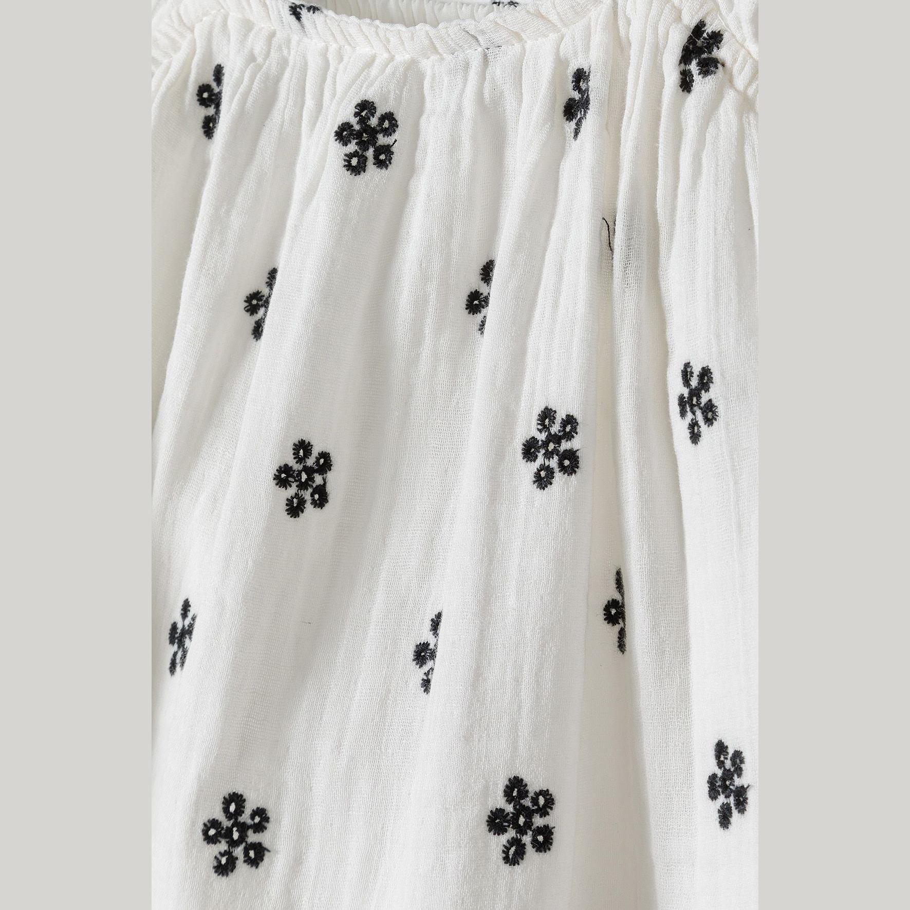 Close-up detail of white fabric showing black embroidered small floral motifs scattered across the dress material