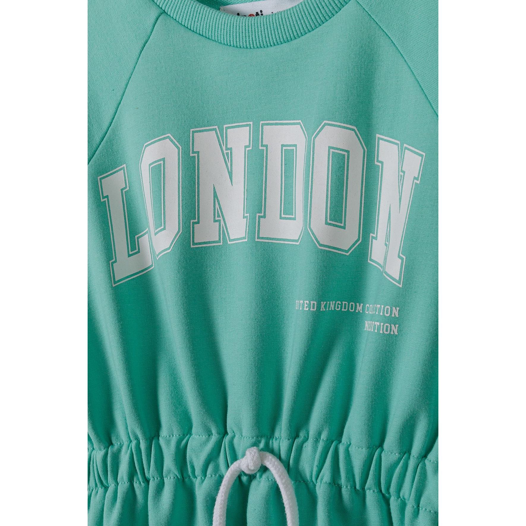 Close-up detail of London print on green fleece fabric showing white lettering and United Kingdom edition text with visible drawstring waist