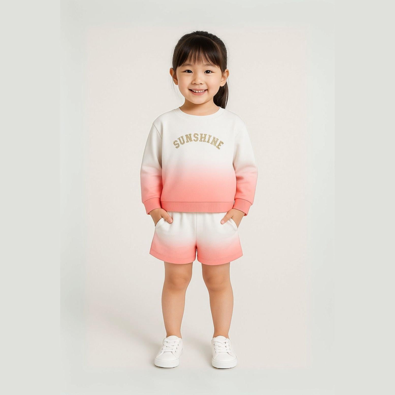 Young girl wearing coral gradient fleece sweatshirt and matching shorts set with SUNSHINE text, standing against neutral background