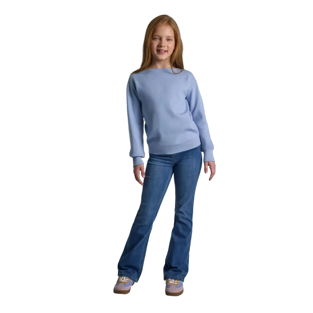 Young girl wearing light blue textured knit jumper with boat neck and jeans, standing against black background