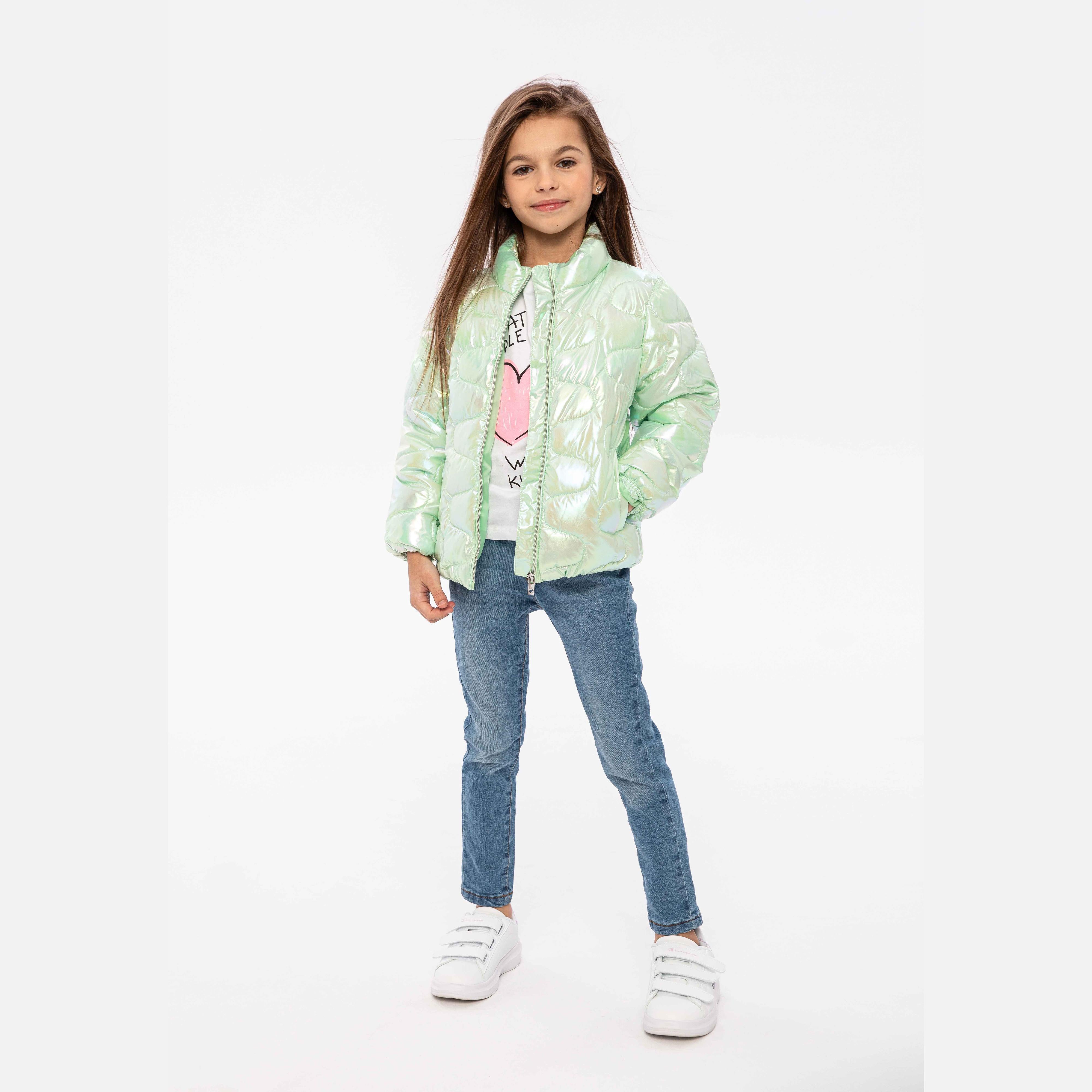 Girl wearing mint green iridescent quilted jacket over white top and jeans, standing against white background