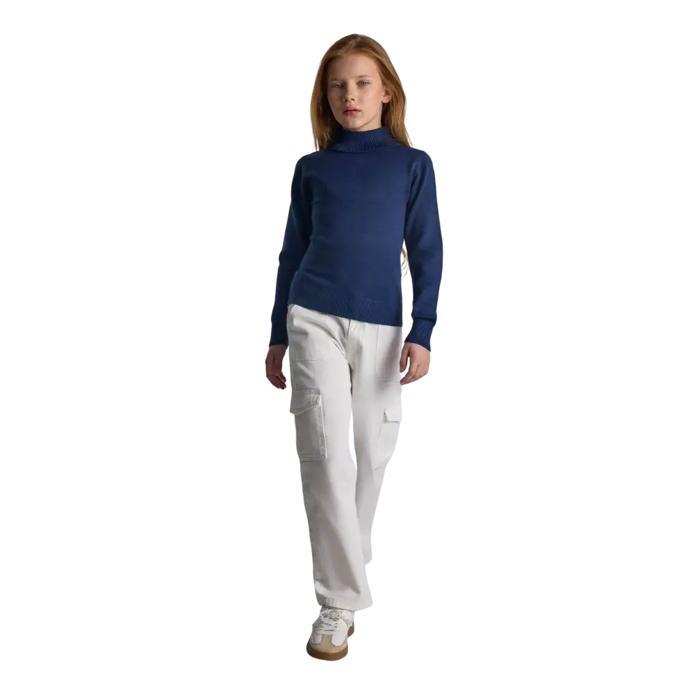 Young girl wearing navy fine knit turtleneck jumper with white cargo trousers and white trainers against black background, full body front view showing classic styling