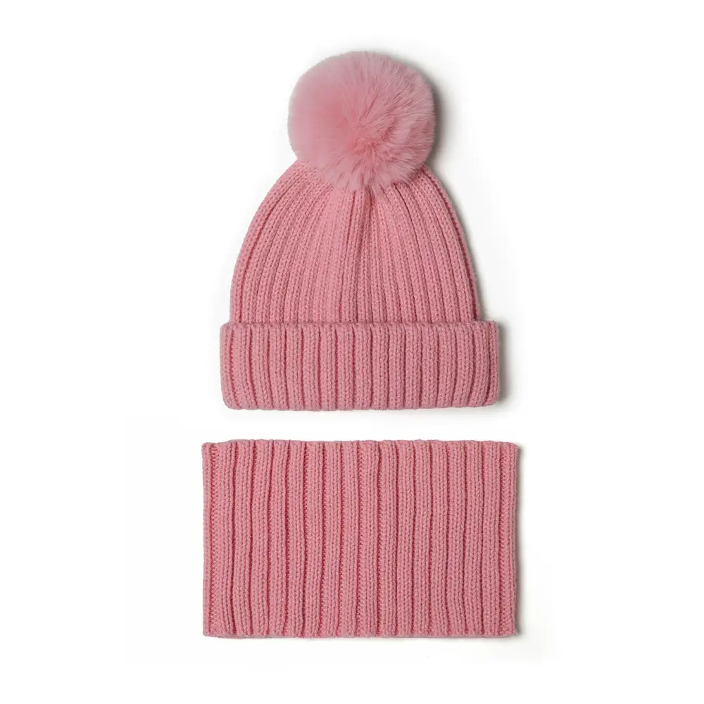 Close-up detail of pink faux fur pompom attached to ribbed knitted hat showing fluffy texture and secure attachment against white background